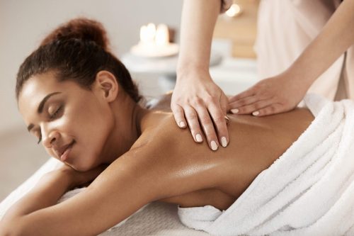 Attractive african girl having massage relaxing in spa salon. Closed eyes.